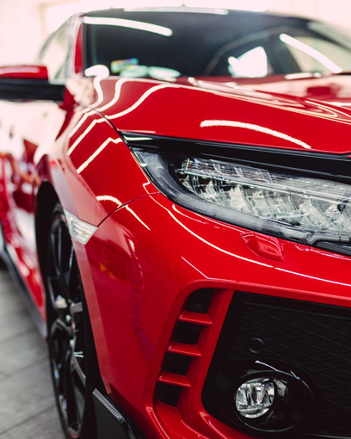 Detailer polishing a red sports car under controlled lighting inside the Apex Detail Co. studio
